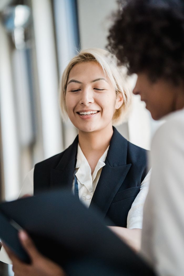 Two women in professional attire discuss a document in a modern office setting.
